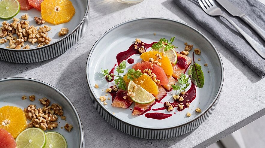 Teller mit Zitrus-Salat: segmentierte Orangen, Grapefruit und Limette, rote Beerensauce, zerkrümelte Walnüsse und frisches Mikrogrün dekorativ angerichtet.
