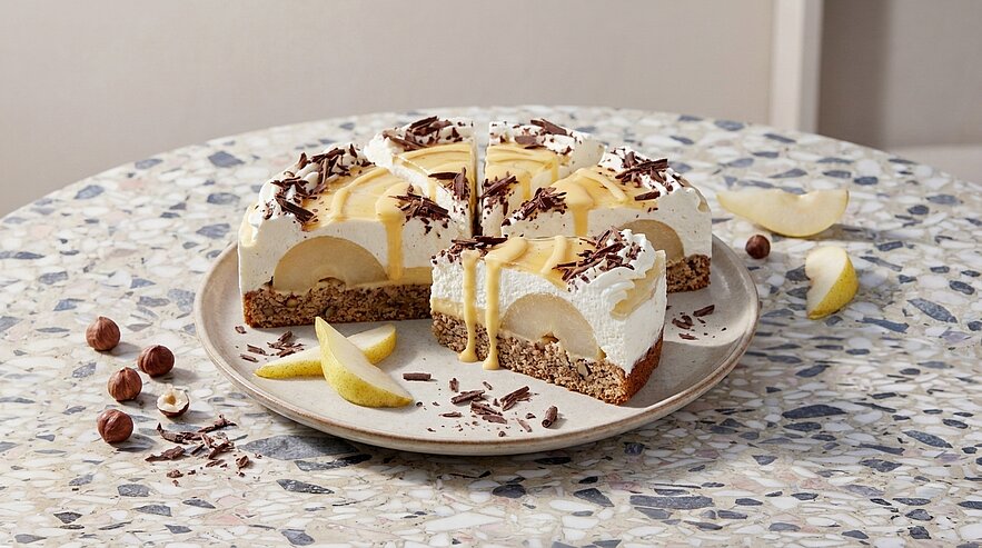 Eine Schnittansicht einer Torte auf einem runden Teller, mit einer cremigen Schicht und dekoriert mit Schokoladenraspeln und Birnenscheiben. Die Torte hat einen Boden aus Keksen und zeigt eine üppige Füllung aus Früchten und Sahne.