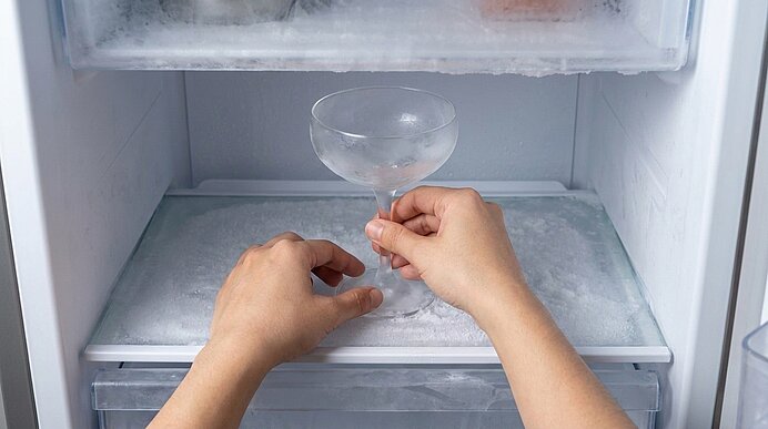 Zwei Hände legen ein eiskaltes Coupé-Glas in einen vereisten Gefrierschrank.