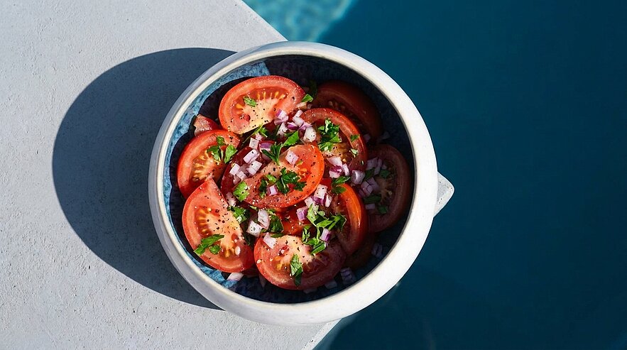 Tomatensalat in einer Schüssel: frische Tomatenscheiben mit gehackter roter Zwiebel, Petersilie und Gewürzen.