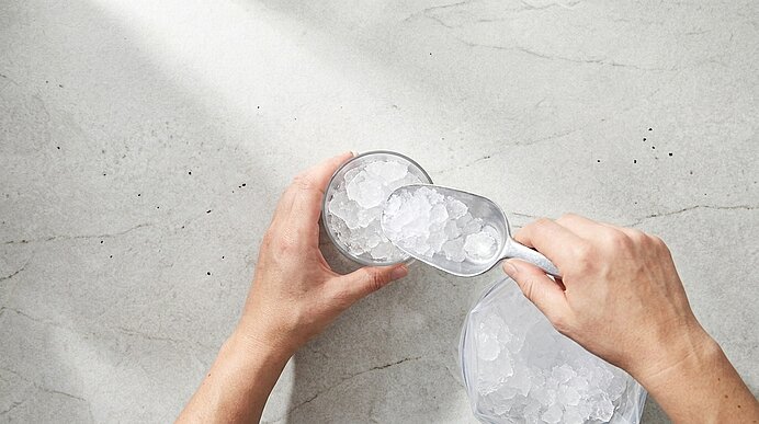 Zwei Hände füllen mit einer Eisschaufel ein Metallglas mit zerstoßenem Eis.