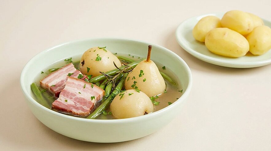 Schüssel mit pochierten Birnen in klarer Brühe, grünen Bohnen, Speckscheiben und Kräutern; daneben kleiner Teller mit gekochten Kartoffeln.