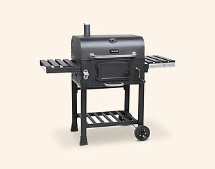 Ein schwarzer Grill mit zwei seitlichen Ablageflächen und einem Untergestell auf Rollen. Der Grill hat eine geschlossene Kammer mit einer Tür und einem Kamin auf der Oberseite. Die Konstruktion ist stabil und eignet sich für das Grillen im Freien.