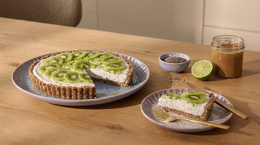Ganze Tarte auf Teller mit knusprigem Boden, weißer Chia-Creme und dünn aufgeschnittenen Kiwi-Scheiben; ein Stück herausgeschnitten und auf einem separaten Teller mit Gabel serviert.