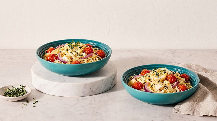 Zwei Schalen mit Pasta sind auf einem marmorierten Tisch platziert. Die blaue Schale enthält Spaghetti mit Kirschtomaten und frischen Kräutern. Neben den Schalen liegt ein kleines Schälchen mit frischem Thymian. Der Hintergrund ist neutral und hell.
