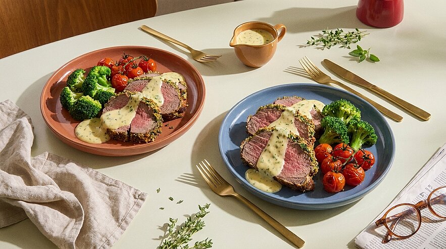 Zwei Teller mit in Scheiben geschnittenem Rinderbraten, darüber Kräuter-Sahnesoße, dazu gedämpfter Brokkoli und geröstete Kirschtomaten.