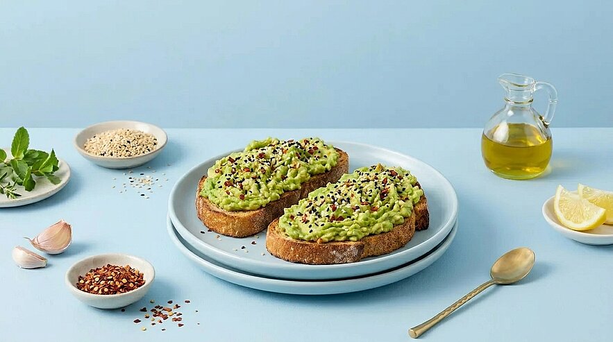 Zwei Scheiben geröstetes Brot mit zerdrückter Avocadocreme, mit Samen und Gewürzen bestreut und auf einem Teller angerichtet.