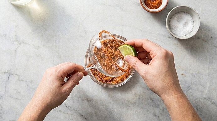 Zwei Hände geben Limettensaft und Öl in eine kleine Glasschüssel mit roter Gewürzmischung und verrühren sie.