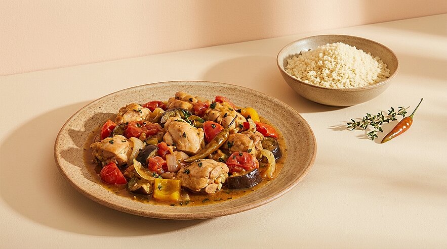 Teller mit Hähnchen-Gemüse-Ragout (Paprika, Aubergine, Tomaten) und daneben eine Schale mit Couscous.