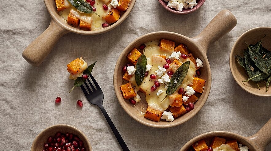 Kleine Schälchen mit gerösteten Süßkartoffelwürfeln, geschmolzenem Käse, Salbeiblättern, Granatapfelkernen und zerbröseltem Feta.