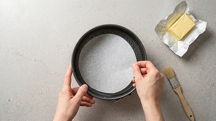 Hände legen ein rundes Backpapier in eine Springform, die zum Backen vorbereitet wird.