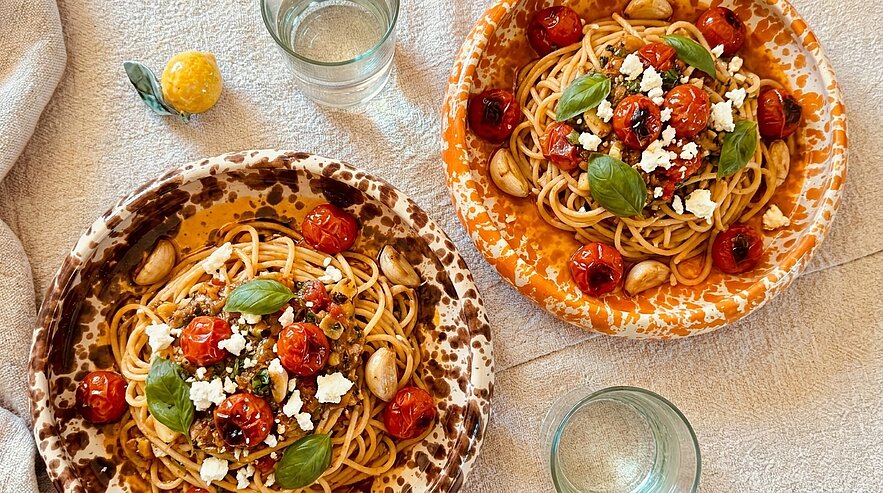 Zwei Schalen Spaghetti mit gerösteten Kirschtomaten, frischen Basilikumblättern und zerbröckeltem Schafskäse, serviert in gemusterten Tellern.