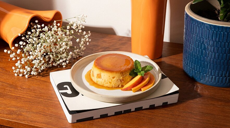 Teller mit Crème caramel (Karamellpudding) in glänzender Karamellsoße, garniert mit Orangenscheiben und einem Minzblatt.