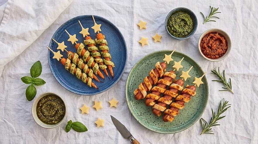 Zwei Teller mit Sternspießen: spiralgewickelte Teig- oder Wurstspieße, serviert mit grünem Pesto- und rotem Dip.