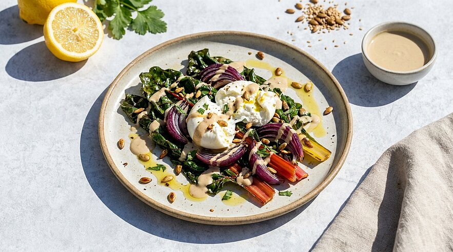 Teller mit cremiger Burrata auf buntem Mangold und Spinat, roten Zwiebelringen, gerösteten Kernen und leichtem, cremigem Dressing.