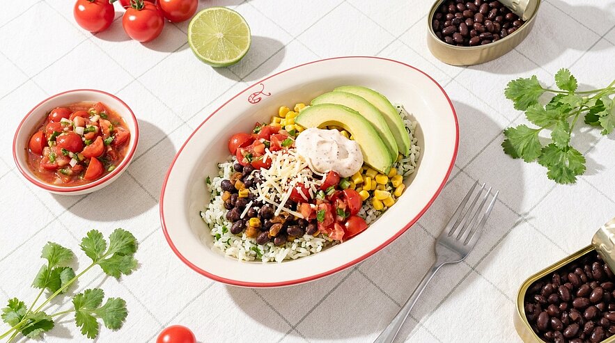 Schüssel mit Reis-Bowl: Reis, schwarze Bohnen, Mais, frische Tomatensalsa, Avocadoscheiben, Klecks Sauerrahm und geriebener Käse.
