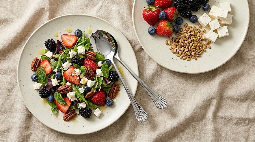 Teller mit buntem Sommersalat aus Erdbeeren, Brombeeren und Blaubeeren, Fetawürfeln, Pekannüssen, Blattsalat und Minzblättern; daneben ein kleiner Teller mit Beeren, Feta und Kernen.