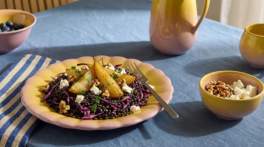 Teller mit Salat aus Rotkohl und schwarzen Linsen, garniert mit gebratenen Birnenspalten, zerbröseltem Feta und Walnüssen.