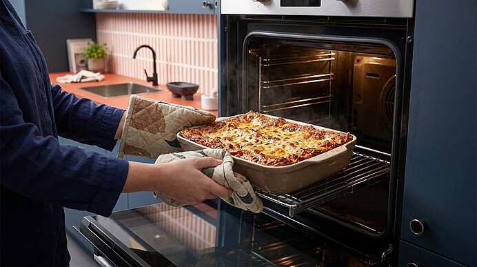 Person nimmt frisch gebackene Lasagne in Auflaufform mit Topflappen aus dem Ofen.