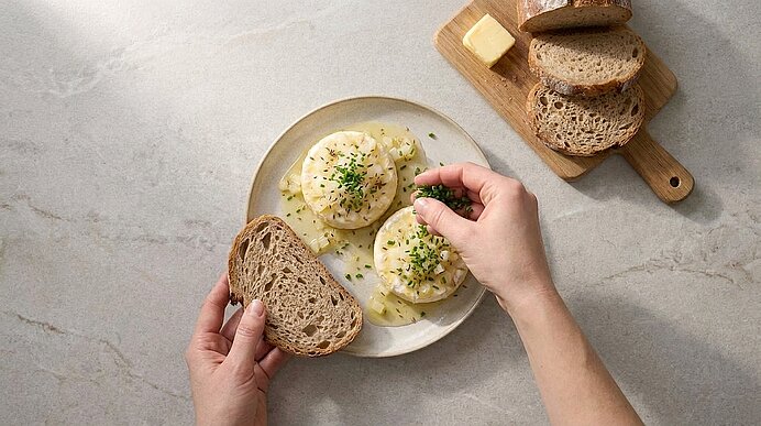 Hände bestreuen zwei mit Mayonnaise und Schnittlauch garnierte halbe Eier auf einem Teller; eine Hand hält eine Scheibe Vollkornbrot. Im Hintergrund ein Brett mit weiteren Brotscheiben und Butter.