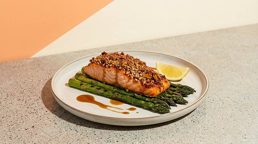 Gebratener Lachs mit knuspriger Kruste auf gebratenem grünem Spargel, serviert mit Zitronenschnitz und leichter Sauce.