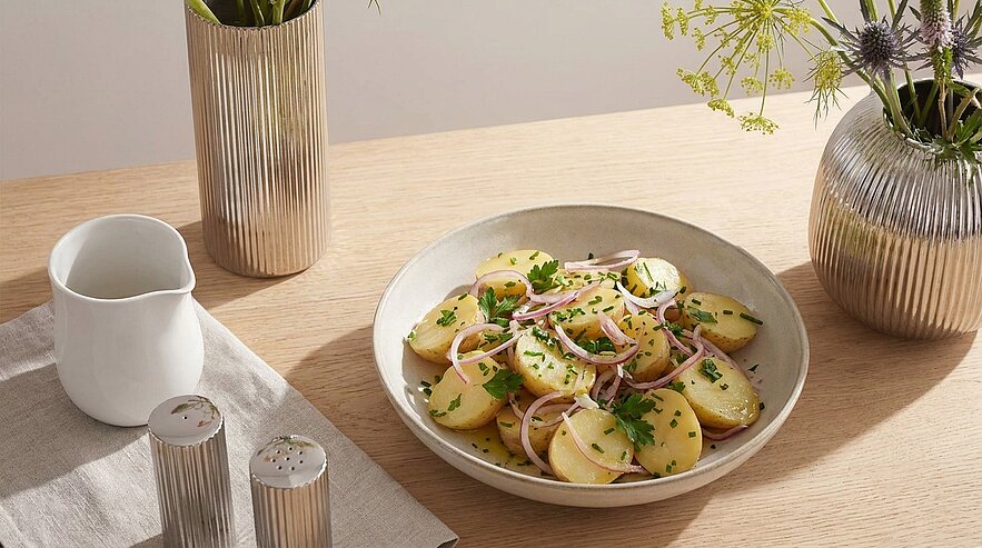 Teller mit Kartoffelsalat aus dünn geschnittenen Pellkartoffeln, roten Zwiebelringen, gehackter Petersilie und leichter Vinaigrette.