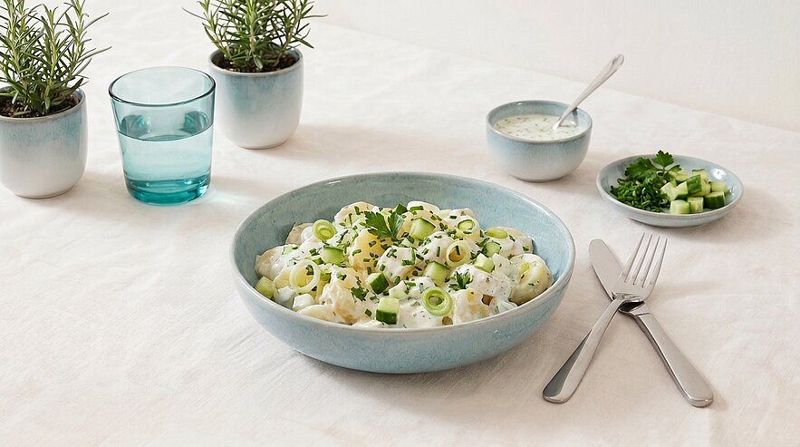 Schale mit cremigem Kartoffelsalat, garniert mit Frühlingszwiebeln und gehacktem Schnittlauch.
