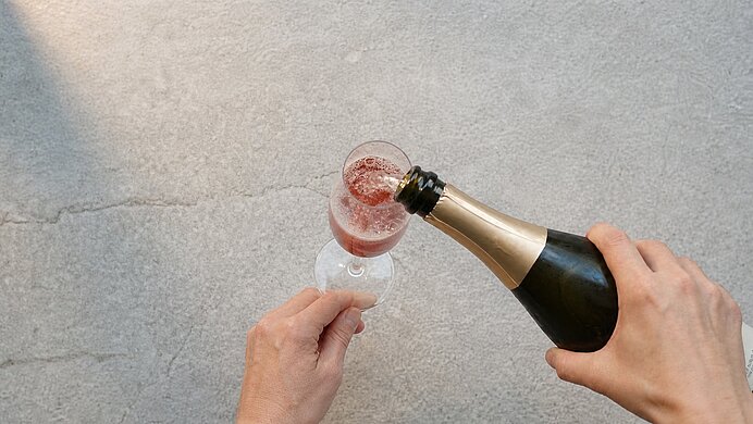Zwei Hände gießen aus einer Sektflasche roséfarbenen Schaumwein in ein Sektglas.