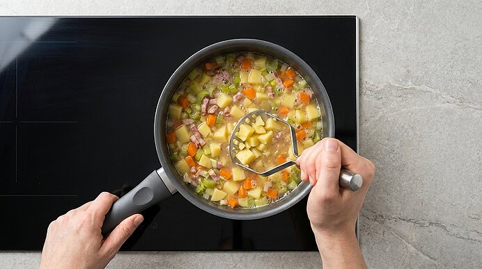 Zwei Hände halten einen Topf auf dem Herd; eine Schöpfkelle hebt eine klare Gemüsesuppe mit Kartoffel-, Karotten- und Selleriewürfeln sowie Schinkenstücken.