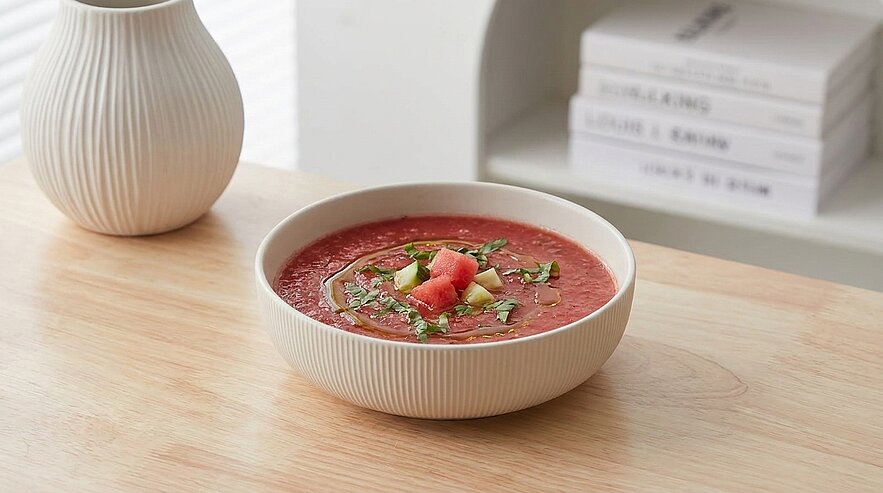 Schale mit roter Gazpacho (kalte Tomatensuppe), garniert mit gewürfelter Gurke, Tomatenstücken, etwas Olivenöl und frischem Basilikum.
