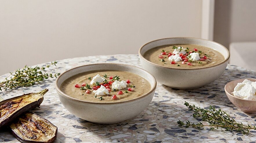 Zwei Keramikschalen mit cremiger Suppe, garniert mit Kräutern, kleinen Tomatenwürfeln und einem Klecks Frischkäse.