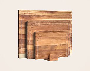 Drei Holzschneidebretter in verschiedenen Größen sind zusammen angeordnet. Vor ihnen steht ein edler Holzhalter. Die Bretter zeigen eine schöne Maserung und natürliche Farben, ideal für die Küche.