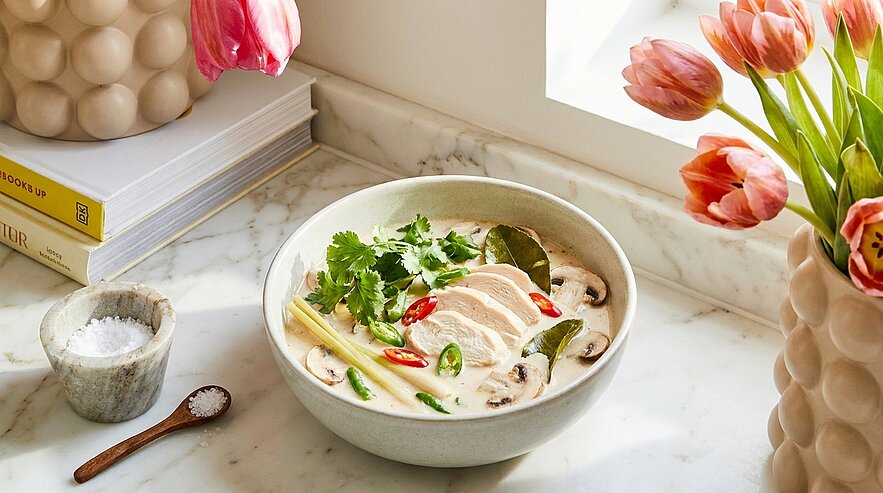 Schale mit cremiger asiatischer Kokosmilchsuppe (Tom Kha) mit dünn geschnittenem Hähnchen, Champignons, Zitronengras, Limettenblättern, roten und grünen Chili und frischem Koriander.