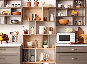 Eine moderne Küche mit Holzregalen und verschiedenen Küchenutensilien. In den Regalen stehen Schalen, Tassen, Obst und Pflanzen. Auf der Arbeitsfläche befinden sich ein Mikrowelle, ein Stapel Teller und eine Schüssel mit Brot. Die Atmosphäre wirkt einladend und gut organisiert.